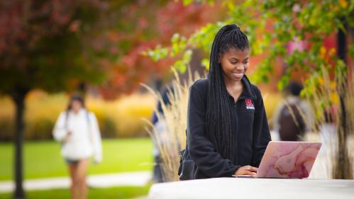 Outdoor Fall scene with a student using a laptop at a table